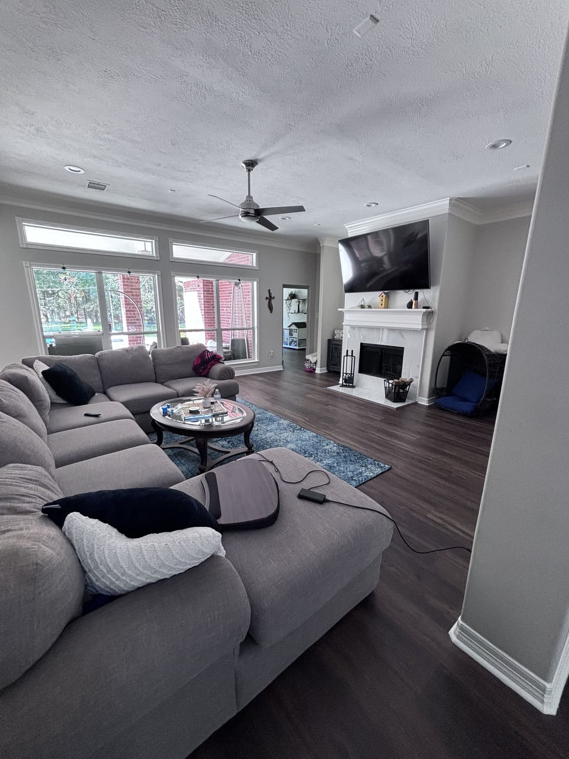 Spacious living room with dark hardwood flooring, a cozy sectional sofa, and a mounted TV above the fireplace. Home remodeling and flooring upgrades available in Pasadena, Spring, and Houston.
