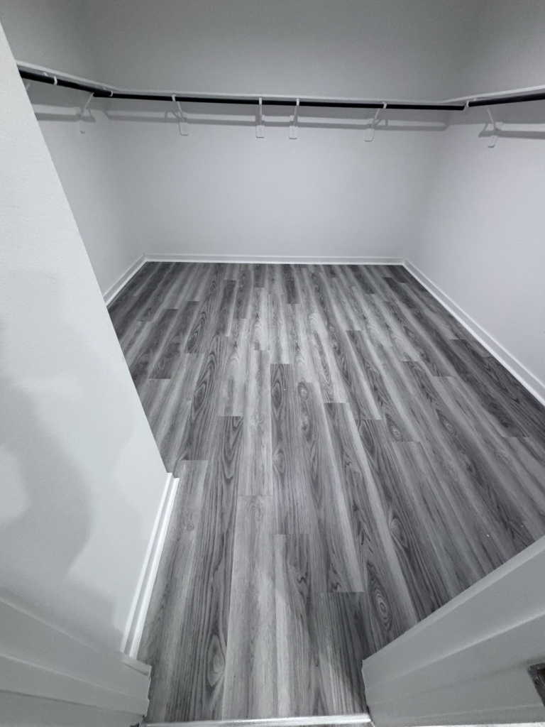 Spacious walk-in closet renovation featuring modern gray wood flooring and custom shelving. Expertly remodeled by a local general contractor serving the Greater Houston Area.
